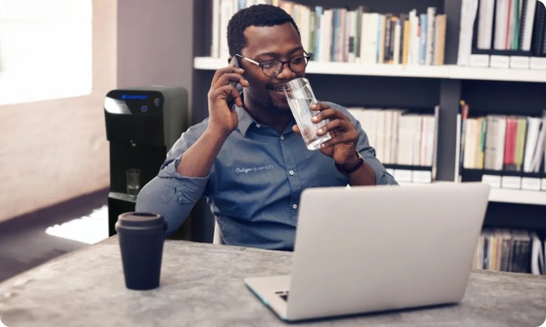 Man drinking water while on phone and staring at laptop